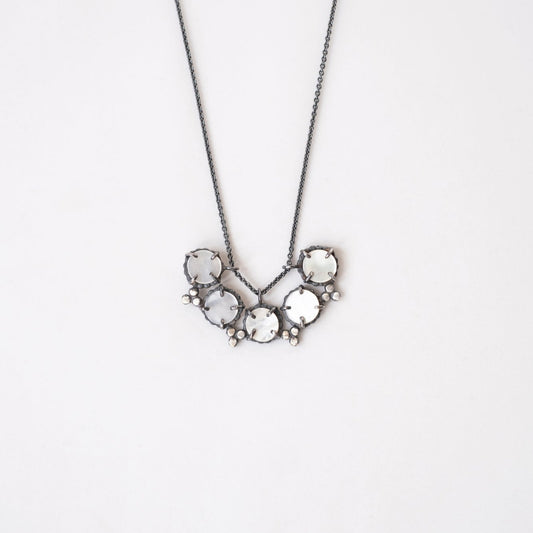 A necklace with a silver chain and a pendant featuring mother of pearl with a star-like pattern, set in black patina sterling silver by Alice Scott
